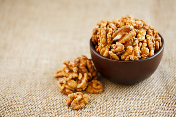 Peeled walnuts in a wooden, dark brown cup on a burlap cloth.