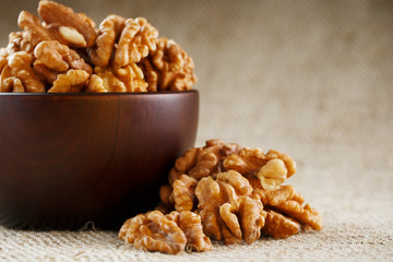 Peeled walnuts in a wooden, dark brown cup on a burlap cloth.