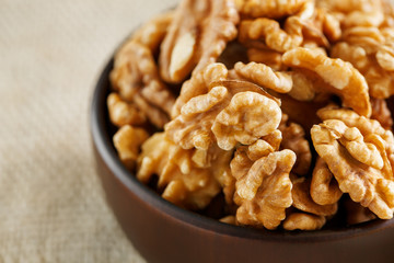 Peeled walnuts in a wooden, dark brown cup on a burlap cloth.