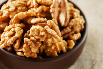 Peeled walnuts in a wooden, dark brown cup on a burlap cloth.