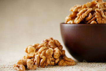 Peeled walnuts in a wooden, dark brown cup on a burlap cloth.