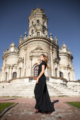Fototapeta premium Young woman in black dress on the background of the church