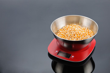 Corn in bowl on an electronic scale on grey mirror background with copy space