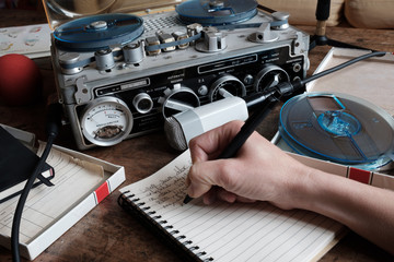 Female hand writing on notebook with tape recorder and microphone, journalist transcribing an interview, close shot