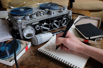 Female hand writing on notebook with tape recorder and microphone, journalist transcribing an interview, close shot