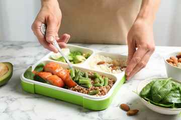 Woman putting natural protein food into container on marble table, closeup