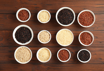 Bowls with different types of rice on wooden background, top view
