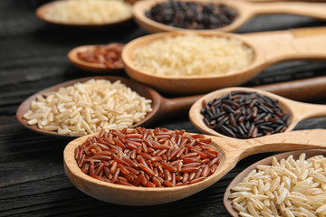 Spoons with different types of rice on wooden background, closeup