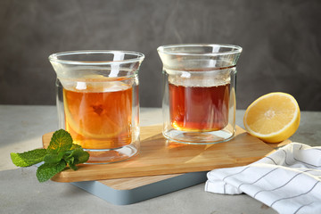 Wooden board with glasses of hot tea and lemon on table