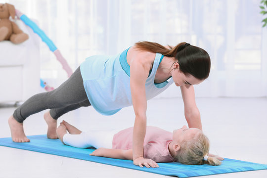 Sportive woman doing fitness exercises with daughter at home
