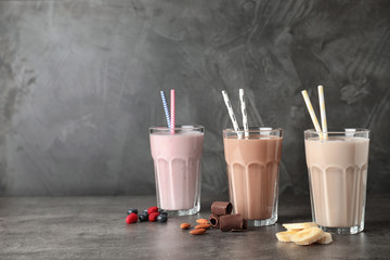 Glasses with different protein shakes and ingredients on table against grey background. Space for...