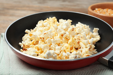 Frying pan with tasty popcorn on table
