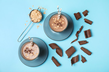 Glasses of chocolate protein shake and ingredients on color background, top view