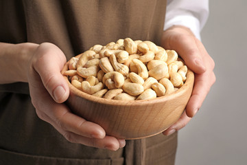 Woman holding bowl of cashew nuts on light background, closeup