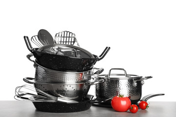 Set of clean cookware, utensils and vegetables on table against white background