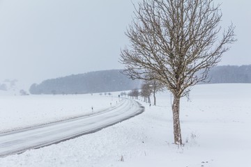 Gefährliche glatte Winter Straße mit Eis wartet auf Winterdienst. Die Fahrbahn ist weiß glatt verschneit. Vorsicht vor Unfall durch Schneesturm und schlechte Sicht. Wetter zur Weihnachten Jahreszeit