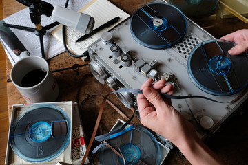 Male hand changing tape on professional portable reel to reel tape recorder, vintage radio journalist, mic, cofee