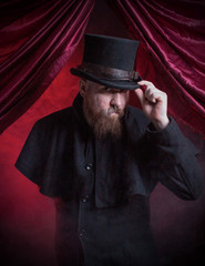 A Magician, wearing a top hat and nodding his head while standing against red background, under red curtains.