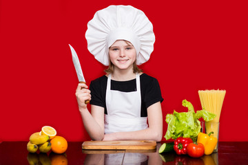 Happy little girl in chef uniform cuts fruit in kitchen. Kid chef. Cooking Concept