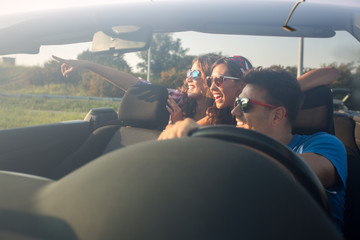 Group of friends driving around in a convertible car while looking at something