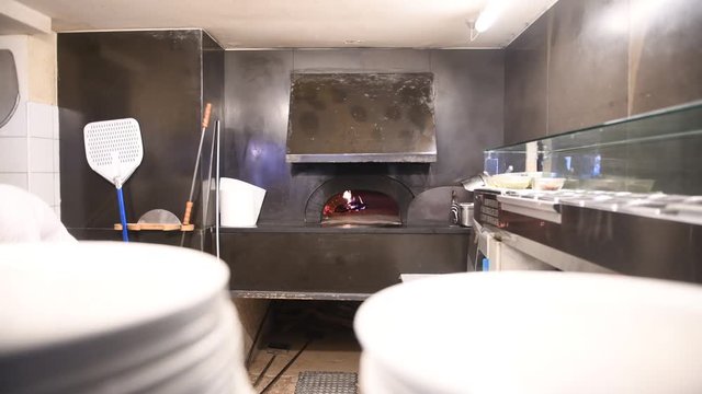 Burning firewood oven in pizza restaurant and empty plates piles