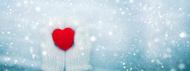 Red heart in woman's hands wearing white woolen mittens. Valentine's Day concept