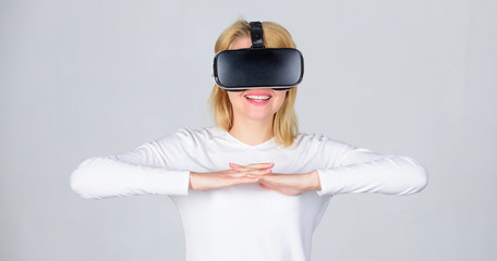 Portrait of an amazed girl using a virtual reality headset isolated on grey background. Woman using VR device. Confident young woman adjusting her virtual reality headset and smiling.