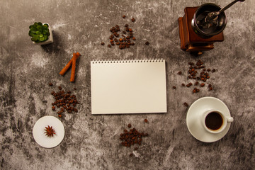 Template mockup clean notebook with cup of coffee, coffee grains, cinnamon, coffee grinder on gray background. View from above. Layout of ideas.