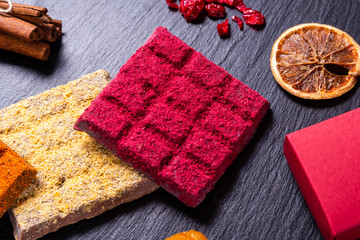 Blocks of homemade chocolates with dried berries on black stone background