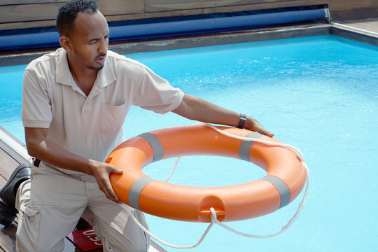 Hands Of The Rescuer With Lifebuoy In Pool. Hotel Worker Throws A Lifeline To A Drowning Pool. Salvation Of A Sinking Person. Life Ring In Swimming Pool. Red Lifebuoy Pool Ring.