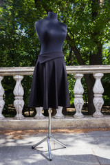 Black skirt on mannequin. Skirt straight cut on background of green trees. Women's skirt in black sewn to order. Tailoring