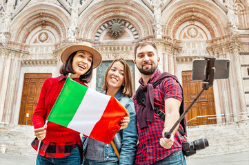 Travel with friends in Italy. Multiethnic diverse group of young people taking selfie in front of a famous landmark the Duomo cathedral in Siena, Tuscany