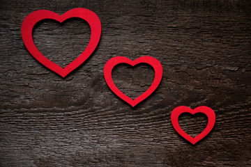 Three red hearts are located diagonally on an old wooden brown wooden board, one smaller than the other. Valentine's Day Card