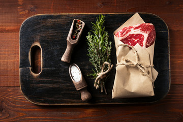 a piece of fresh marbled beef on a wooden background, with spices for cooking steak