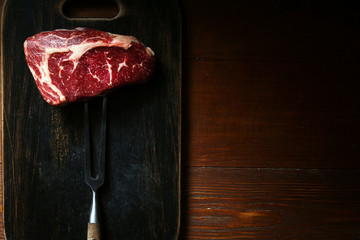 a piece of fresh marbled beef on a wooden background, with spices for cooking steak