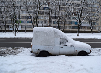 White car in the snow near the asphalt road in the city in winter.