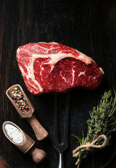 a piece of fresh marbled beef on a wooden background, with spices for cooking steak