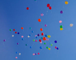 Colorful multicolored inflatable balls fly in air against background blue sky during festive festival