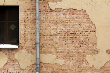Old cracked brick plastered wall of the house and a window with drainpipe. Background. Interior...