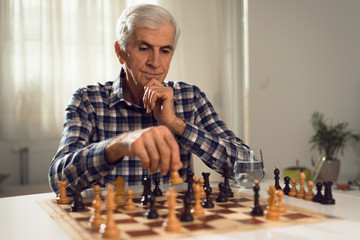 Senior man sitting at home and playing chess by itself.