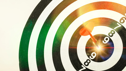 Red dart arrow hitting in the target center of dartboard with Shining light.