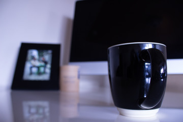 Coffee mug in front of computer screena d blurred family picture in morning light