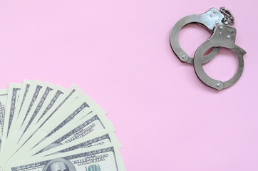 Police handcuffs and hundreds of us dollars lie on a pink background