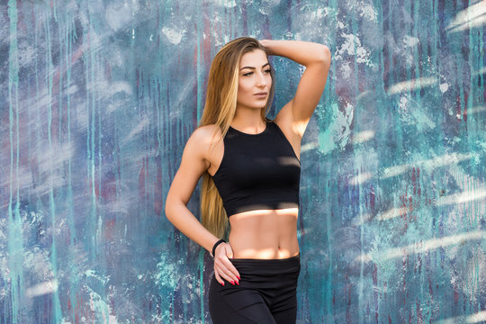 Young beautiful fitness woman wearing sporty clothes tanding against wall. Fitness workout concept.