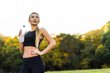 Thirsty woman drinking water to recuperate after jogging in park