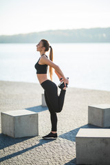 Fototapeta na wymiar Attractive and strong woman stretching legs before fitness on the lake in the summer. Sports concept. Healthy lifestyle