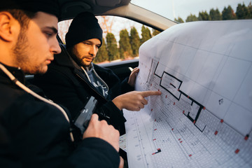 Two robbers planning and pointing on the blueprint(map) their objective while holding their guns.