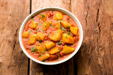 Indian food - Aloo curry masala. Potato cooked with spices and herbs in a tomato curry. served in a bowl over moody background. selective focus