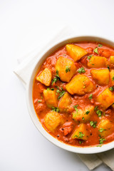 Indian food - Aloo curry masala. Potato cooked with spices and herbs in a tomato curry. served in a bowl over moody background. selective focus