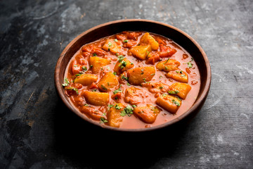 Indian food - Aloo curry masala. Potato cooked with spices and herbs in a tomato curry. served in a bowl over moody background. selective focus